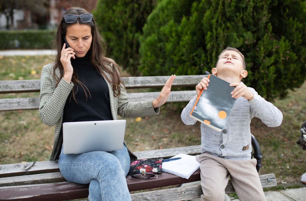 A person talking on a cell phone while sitting on a bench with a child| Why Tantrums Happen.